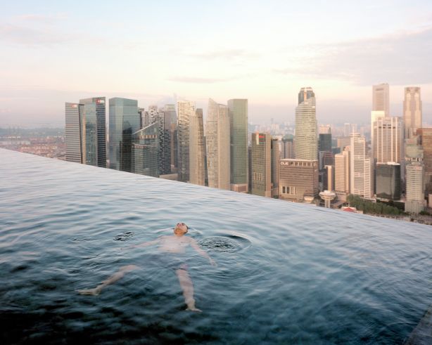 A man floats in the 57th-floor swimming pool of the Marina Bay Sands Hotel, with the skyline of the Singapore financial district behind him. Paolo Woods & Gabriele Galimberti, 2013, INSTITUTE