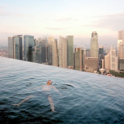 A man floats in the 57th-floor swimming pool of the Marina Bay Sands Hotel, with the skyline of the Singapore financial district behind him. Paolo Woods & Gabriele Galimberti, 2013, INSTITUTE